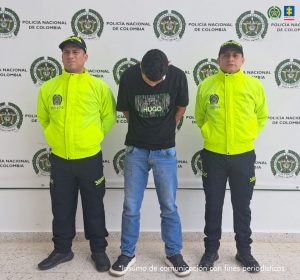 En la fotografía aparece una persona capturada en compañía de uniformados de la Policía Nacional. En la parte posterior un banner con logos de la entidad.