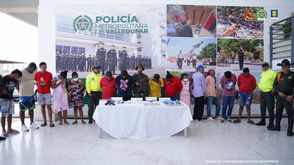En la fotografía aparecen 14 personas capturadas, acompañadas de uniformados del Gaula Militar y de la Policía Nacional. En la parte posterior un banner con logos de la entidad.