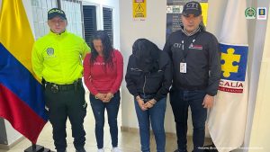 En el centro se ven dos mujeres capturadas. De un lado un directivo del Cuerpo Técnico de Investigación del CTI y del otro de la Policía Nacional. Detrás de las banderas de la Fiscalía General de la Nación y la de Colombia Pie de foto: Lady Johanna Vargas Rojas y Diana Marcela Ruiz Rojas fueron privadas de su libertad