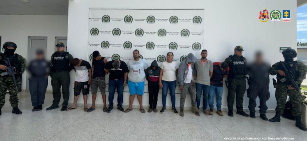 En la fotografía aparecen nueve personas capturados en compañía de servidores del CTI, y de uniformados de la Policía y el Ejército Nacional. En la parte posterior un banner con logos de la entidad. 