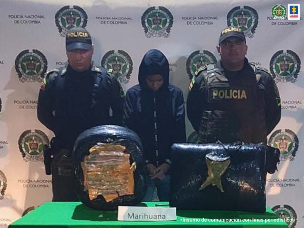 En la foto aparece, de pie y con los brazos adelante, Laura Alejandra Rengifo Plaza. Viste chaqueta oscura con capucha y pantalón oscuro. A lado y lado de ella hay uniformados de la Policía Nacional. Delante de ellos hay una mesa con mantel verde y sobre ella hay un morral abierto donde se ve un paquete color café claro; al lado del morral se ve un paquete cuadrado, envuelto en plástico negro, así como un letrero que dice: ‘Marihuana’. Detrás de ellos hay un pendón institución de la Policía.