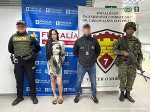capturada de frente custodiada por un investigador del CTI de la Fiscalía, un policía y un militar. Detrás banner de Fiscalía y Ejército.