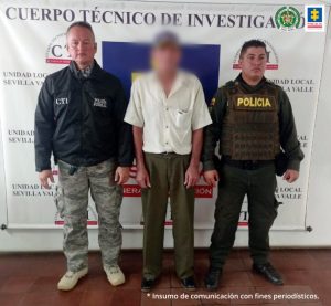 En la fotografía se aprecia a Laureano Torrejano Figueroa, de pie. Viste camisa de manga corte color beage; pantalón café y zapatos oscuros; asimismo, usa gorra. Al lado derecho de él hay un uniformado del CTI de la Fiscalía y a la izquierda hay un uniformado de la Policía Nacional. Detrás de ellos hay un pendón institucional con logos del CTI y de la Fiscalía.