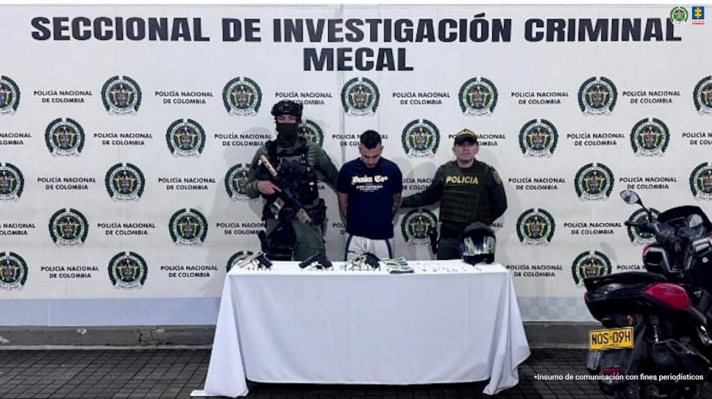 En la fotografía aparece de pie y con los brazos atrás Leider Alexis Lozada Escobar. Viste con camiseta de mangas cortas, de color negro y con estampado blando a la altura del pecho; Asimismo, usa pantalón de sudadera gris con franjas negras a los costados. En sus extremos hay uniformados de la Policía Nacional. Delante de ellos hay una mesa con mantel blanco y sobre ella se aprecian tres armas de fuego, munición, dinero, joyas y un casco. En el extremo derecho de la fotografía se ve una motocicleta. Detrás del imputado hay un pendón institucional de la Policía.