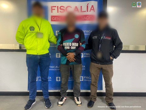 Se visualiza al capturado con el rostro difuminado junto a un integrante de la Policía Nacional y un investigador del CTI. Detrás el banner que identifica a la Fiscalía General de la Nación.