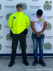 El procesado de camisa blanca, es custodiado por la Policía Nacional. De fondo hay un logotipo de la Dirección de Tránsito y Transporte.