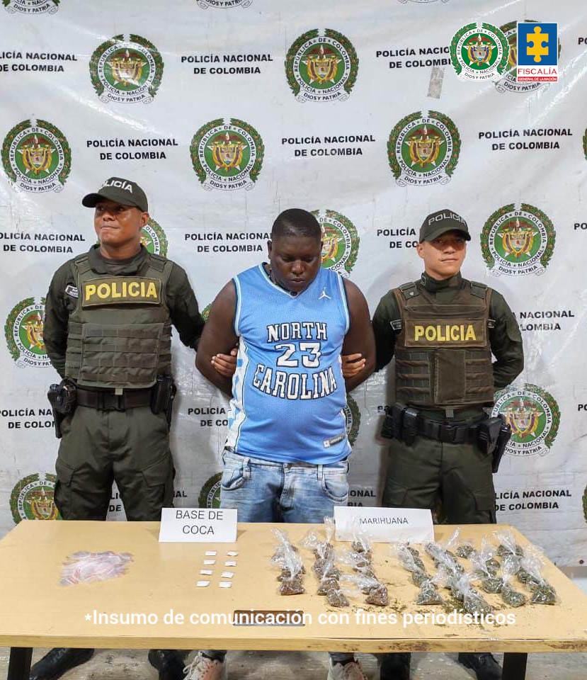 En la fotografía aparece de pie y con los brazos atrás Lewinson Rentería Martínez. Viste camiseta sin mangas de color azul cielo con estampados y ribetes blancos; asimismo, usa jean azul desgastado. A sus extremos hay uniformados de la Policía Nacional. Delante de ellos hay una superficie y sobre ella se aprecian varias bolsas plásticas, así como dos letreros que dicen: ‘Base de coca’, y ‘Marihuana’. Detrás de ellos hay un pendón institucional de la Policía.