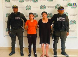 En la fotografía aparecen dos mujeres capturadas, acompañadas de dos uniformados de la Policía Nacional. En la parte posterior un banner con logos de la entidad.