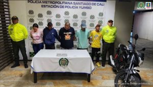 En la fotografía aparecen de frente los presuntos integrantes de ‘Los Abuelos’. A lado y lado de ellos hay uniformados de la Policía Nacional. Delante de ellos hay una mesa con mantel blanco y sobre ella hay un letrero que dice ‘Orden Judicial’. Al lado izquierdo de ellos hay una motocicleta. Detrás de ellos hay un pendón institucional de la Policía.