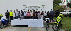 En la foto aparecen de pie los presuntos integrantes de ‘Los Administradores. Al lado derecho hay un uniformado de la Policía. Al lado izquierdo hay un servidor del CTI de la Fiscalía y un uniformado de la Policía. Delante de ellos hay una mesa con mantel blanco y sobre ella hay una pesa, celulares, bolsas plásticas pequeñas, dinero y a los extremos de las mesas hay dos motocicletas. Detrás de ellos hay un pendón institucional de la Policía.