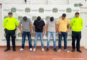 Los capturados se encuentran de frente y custodiados por dos uniformados de la Policía Nacional. Detrás se ve un backing de la Policía Nacional.