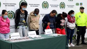 En la fotografía se aprecia de pie a los presuntos integrantes del grupo delincuencial en mención. A sus extremos hay uniformados de la Policía Nacional. Delante de ellos hay una mesa y sobre ella hay una mesa con mantel verde y sobre ella hay paquetes con cigarrillos, bolsas plásticas y dinero en efectivo. Asimismo, se aprecian tres letreros que dicen: ‘Marihuana’, ‘Cocaína’, ‘Dinero’. Detrás de ellos hay un pendón institucional de la Policía.