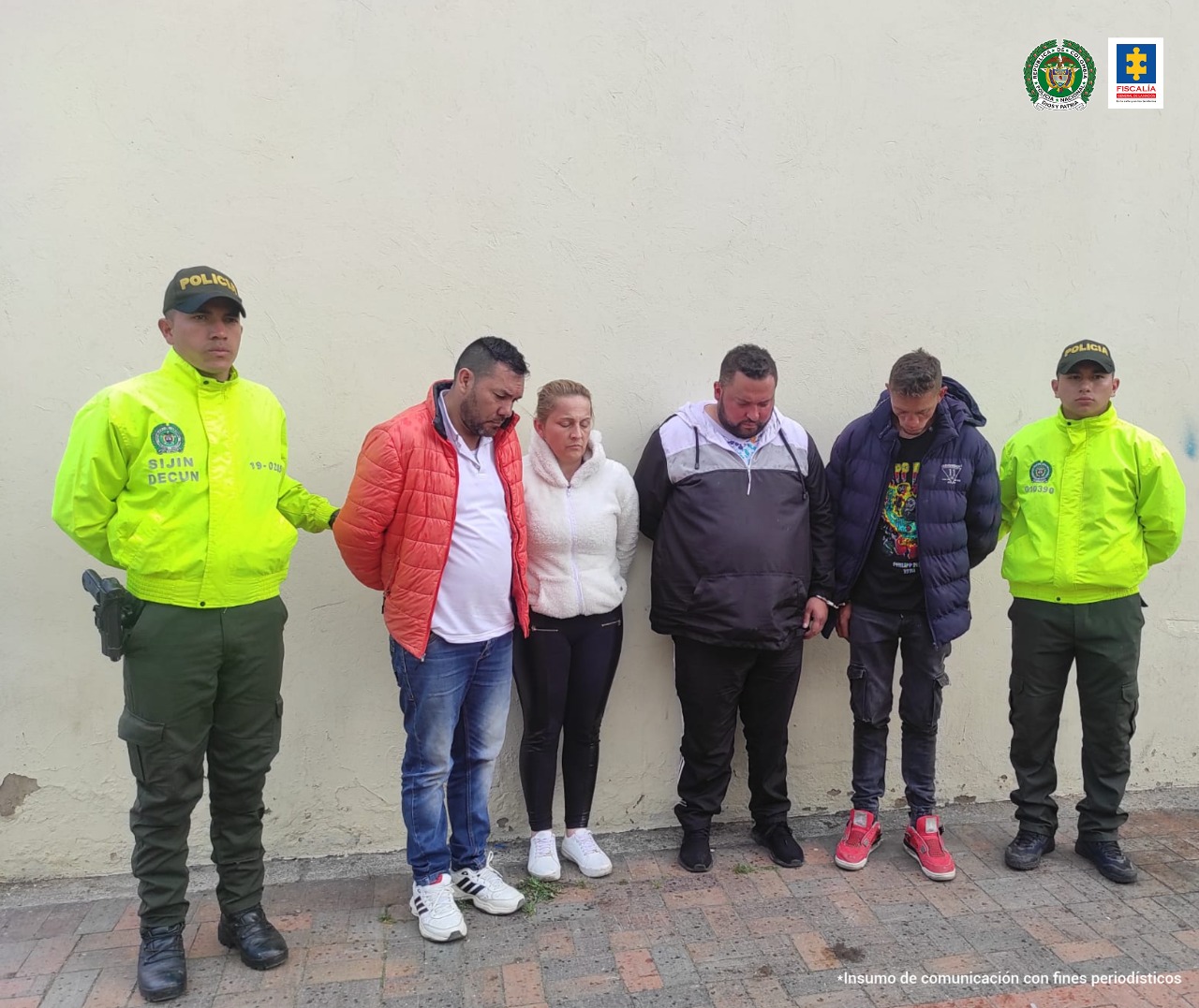 Tres hombres y una mujer capturados, con las manos atrás y acompañados de dos funcionarios de la policía.