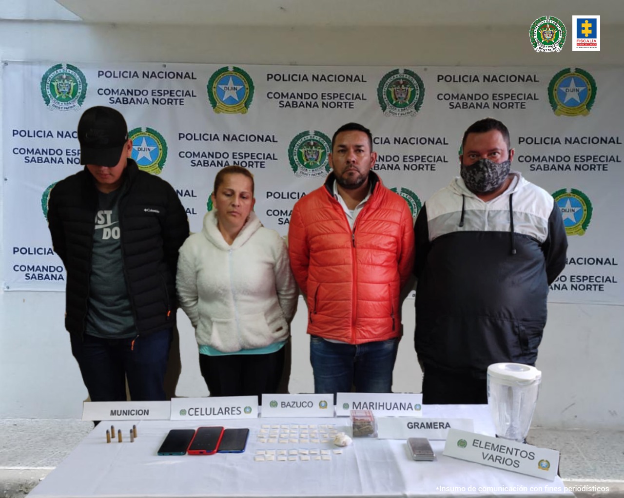 cuatro personas capturadas, en posición de pie. Frente de ellos hay una mesa con tres celulares, estupefacientes y municiones incautados