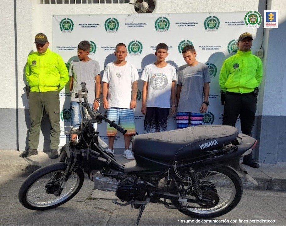 En la foto aparecen cuatro presuntos integrantes de ‘Los Chatarreros’, acompañados a sus lados de dos uniformados de la Policía Nacional. Delante de ellos se ve una motocicleta incautada y detrás de ellos hay un pendón institucional de la Policía Nacional.