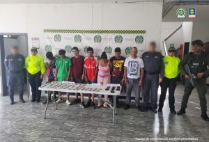En la fotografía se aprecia a los presuntos integrantes de ‘Los Chuncos’. A los extremos de ellos hay servidores del CTI de la Fiscalía y de la Policía Nacional. Delante de ellos hay una mesa y sobre ella hay varias bolsas plásticas con contenido verdoso y oscuro, así como varios teléfonos celulares. Asimismo, hay tres letreros que dicen: ‘Marihuana’, ‘Bazuco’ y ‘Celulares’. Detrás de ellos hay un pendón institucional de la Policía.