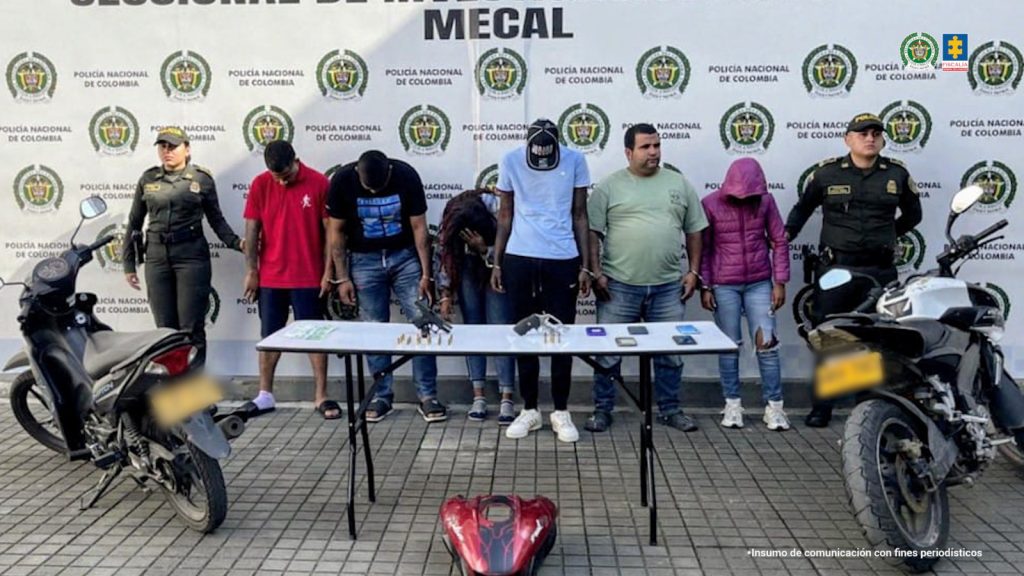 En la fotografía aparecen los seis capturados junto a dos uniformados de la Policía Nacional. En la parte posterior está una mesa con dos armas de fuego, munición dinero, teléfonos celulares y a un lado dos motocicletas