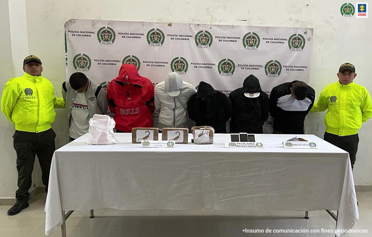 En la fotografía aparecen los 6 capturados junto a dos agentes de la Policía. En la parte posterior se ve una mesa con tres kilos de cocaína, tres teléfonos celulares y un arma de fuego