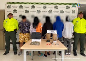 Los imputados se encuentran de espalda y en custodia por dos uniformados de la Policía Nacional. Detrás se observa un backing de la Policía.