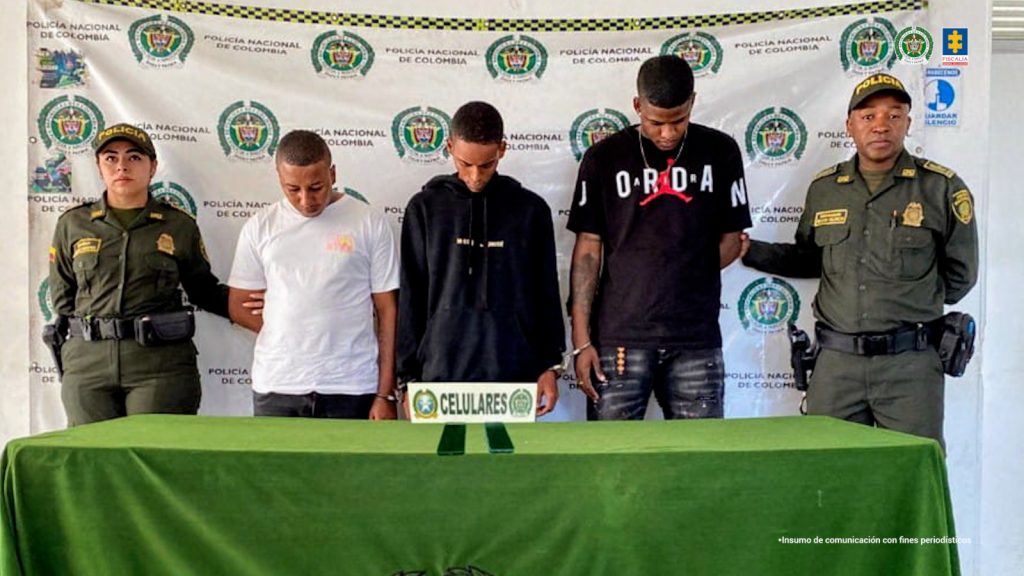 En la fotografía aparecen los tres capturados junto a un funcionario del CTI y un integrante de la Policía Nacional. En la parte superior está un banner de la Fiscalía General