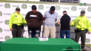 En la fotografía se aprecia, de pie a los tres presuntos integrantes de ’Los Gordos’. Uno de ellos de espalda a la cámara. Uno viste camiseta de manga corta color marrón y jean azul desgastado; otro viste camiseta de manga corta azul claro y pantalón caqui. El otro viste camiseta de manga corta negra con mangas blancas y jean azul. A sus extremos hay uniformados de la Policía Nacional. Delante de ellos hay una mesa con mantel verde y sobre ella un letrero que dice: ‘Orden judicial’. En la parte posterior hay un pendón institucional de la Policía.