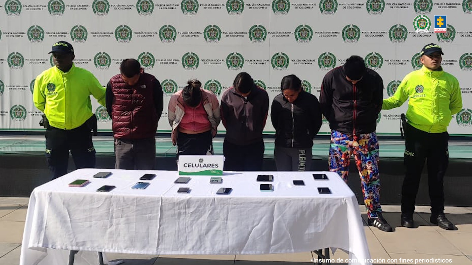 En la fotografía se ven siete personas, cinco de ellas los capturados y dos uniformados de la Policía Nacional. En la parte posterior se ve un backing con escudos de la Policía Nacional. 