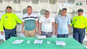 En la imagen se ven los tres capturados en custodia por dos uniformados de la Policía Nacional. En la foto también se ve una mesa donde están los billetes de lotería que usaban para cometer los hurtos.