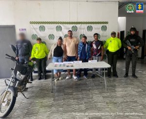 En la fotografía se aprecia a cuatro presuntos integrantes de ‘Los Piñeres’. Entre ellos hay una mujer. Al extremo derecho de ellos hay un servidor del CTI de la Fiscalía y un uniformado de la Policía Nacional. Al extremo izquierdo hay dos uniformados de la Policía. Delante de ellos hay una mesa de superficie blanca y sobre ella hay dinero en efectivo, celulares y bolsas plásticas transparentes. Asimismo, hay cuatro letreros que dicen: ‘Dinero’, ‘Elementos varios’, ‘Clorhidrato de cocaína’ y ‘Bazuco’. Detrás de ellos hay un pendón institucional de la Policía.