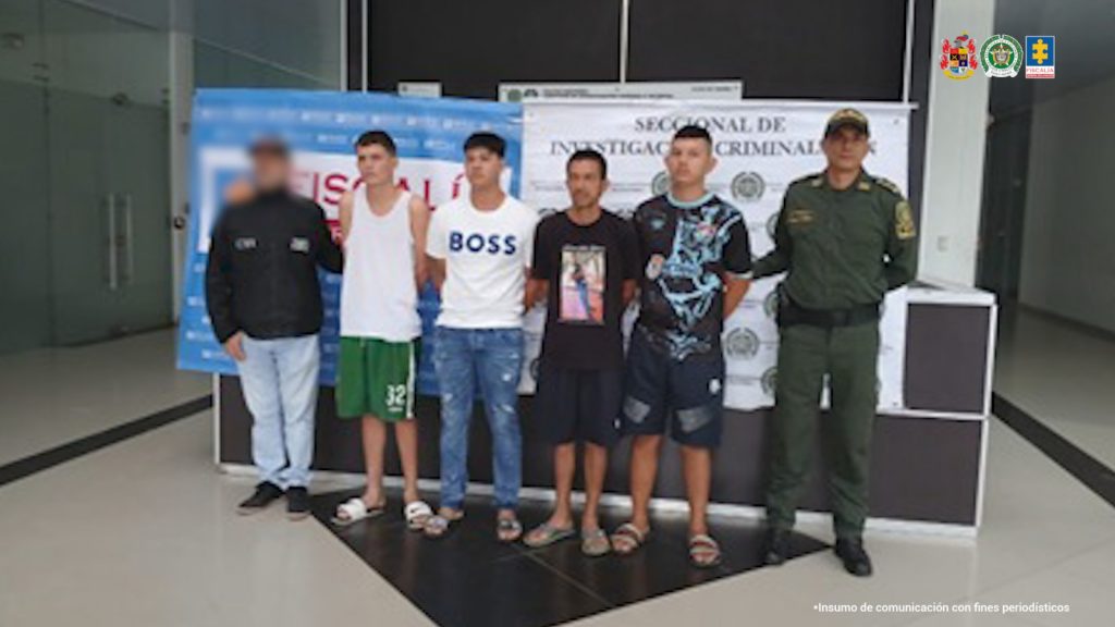 Se visualiza a los capturados junto a un investigador del CTI y un uniformado de la Policía Nacional. Detrás de ellos los banners de la Fiscalía General de la Nación y de la Policía Nacional.