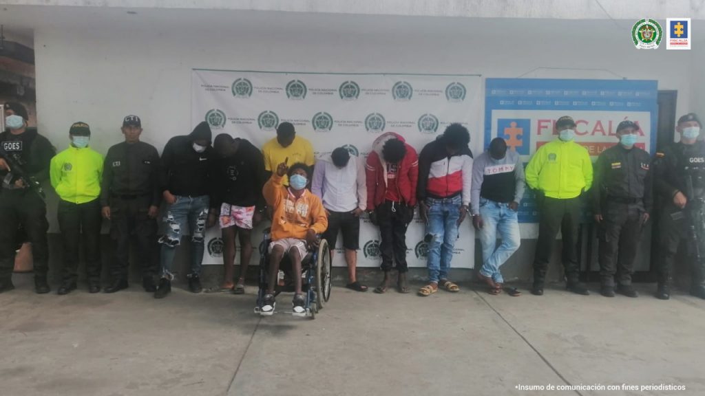 En la foto aparecen los presuntos integrantes de ‘Los Tatos’, uno de ellos en silla de ruedas, acompañados a su derecha por un uniformado de la Policía Nacional y a su izquierda de un servidor del CTI de la Fiscalía. Detrás de ellos hay dos pendones institucionales de la Fiscalía y la Policía Nacional.