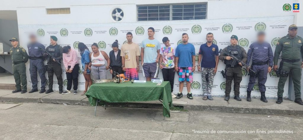 En la fotografía aparecen de pie y en hilera los presuntos integrantes de Los Urbanos. Entre ellos hay cuatro mujeres. A los extremos hay servidores del CTI de la Fiscalía y la Policía Nacional. Delante de ellos hay una mesa, con mantel de color verde y sobre ella se aprecias unos elementos. Detrás de ellos hay un pendón de la Policía.