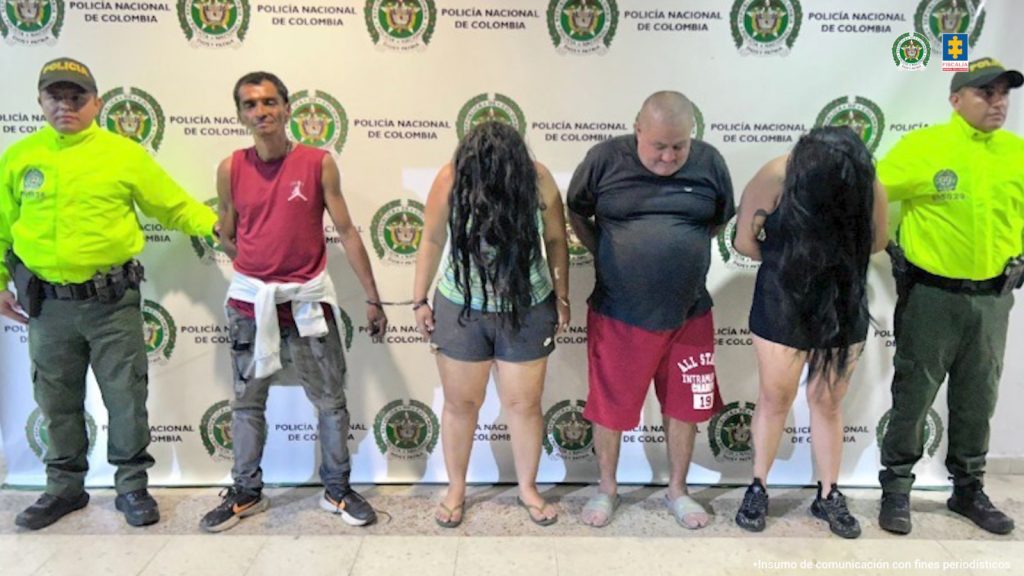 Los imputados se encuentran custodiados por dos uniformados de la Policía Nacional. Detrás se observa un backing de la Policía.