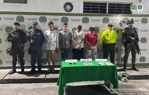En la fotografía se aprecia a los presuntos integrantes del grupo delincuencial ‘Los De San Pacho’. Al lado derecho de ellos hay un servidor del CTI de la Fiscalía y de la Policía Nacional. Al lado izquierdo de ellos hay dos uniformados de la Policía. Delante de ellos hay una mesa con mantel verde y sobre ella hay tres letreros que dicen: ‘Celulares’, ‘Clorhidrato de cocaína’ y ‘Dinero’. Asimismo, hay elementos alusivos a dichos letreros. Detrás de los hoy imputados hay un pendón institucional de la Policía.