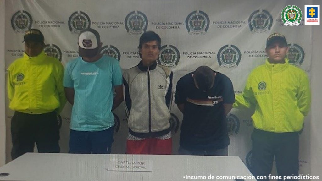 En la foto aparecen los presuntos integrantes de ‘Los del Callejón’, con los brazos atrás, y lado y lado de ellos hay dos uniformados de la Policía Nacional. Delante de ellos hay una mesa blanca con un aviso que dice ‘capturados con orden judicial’. Detrás de ellos hay un pendón institucional de la Policía.