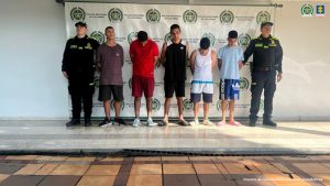 En la foto aparecen cinco de los capturados de frente y custodiados por uniformados de la Policía Nacional. Detrás hay un backing de la Policía Nacional.