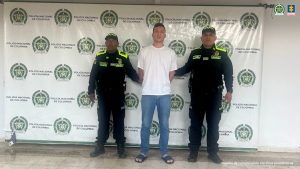 En la foto aparece uno de los capturados de frente con buso blanco y custodiados por uniformados de la Policía Nacional. Detrás hay un backing de la Policía Nacional.