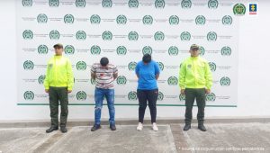 en la imagen se ve una pareja detenida bajo custodia de dos uniformados de la Policía.