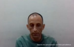 El hombre aparece solo en la fotografía, sentado, solo se ve desde sus hombros hasta su cabeza. Al fondo se ve una pared blanca.