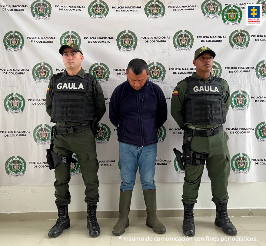 El detenido aparece en el centro de la imagen, a ambos costados suyos hay dos personas de la policía.