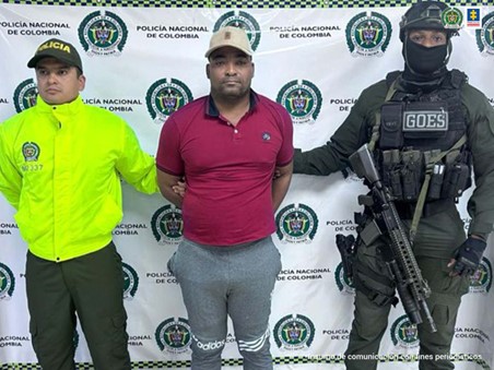 En la fotografía aparece un hombre capturado junto a dos uniformados de la Policía Nacional. En la parte posterior se ve un banner de la Policía Nacional.