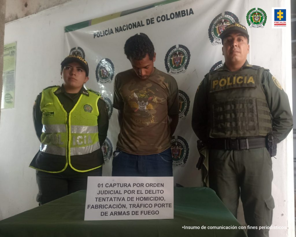 En la fotografía se aprecia a Luis Ángel Díaz Lenis, de pie, con los brazos atrás y la cabeza agachada. Viste camisa de manga corta con estampado militar con estampado; jean oscuro. A lado y lado de él hay uniformados de la Policía Nacional. Delante de ellos hay una superficie verde y sobre ella un letrero que dice: ’01 captura por orden judicial por el delito tentativa de homicidio, fabricación, tráfico, porte de armas de fuego’. Detrás de ellos hay un pendón institucional de la Policía.