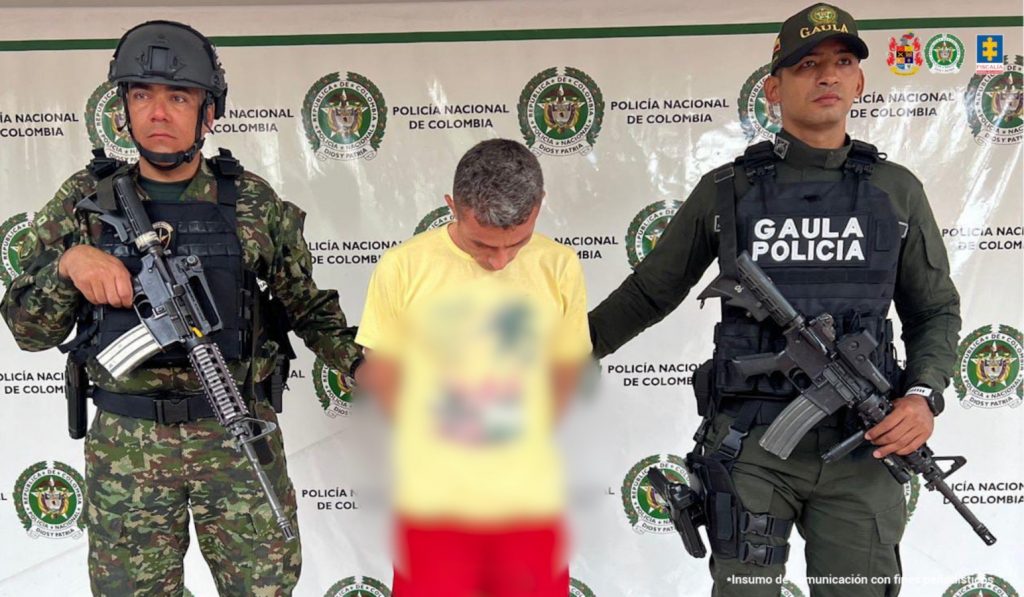 El imputado se encuentra en custodia por uniformados del Gaula de la Policía y Ejército Nacional. Detrás se observa un backing de la Policía.