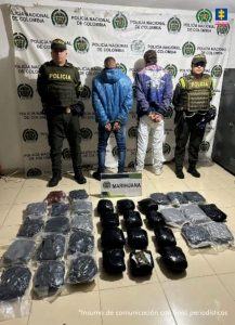 En la fotografía se aprecian de pie, con los brazos atrás, esposados y de espaldas a la cámara a Luis David Mosquera Herrera y José Antonio Vargas Grijalba. Uno viste chaqueta azul con capucha; jean azul y zapatos negros. El otro viste con chaqueta morada y estampado blanco con rosado en la parte superior de la espalda; así como jean azul claro y tenis blancos. A sus extremos hay uniformados de la Policía Nacional. En el suelo hay varios paquetes y un letrero que dice: ‘Marihuana’. En la parte posterior hay un pendón institucional de la Policía.