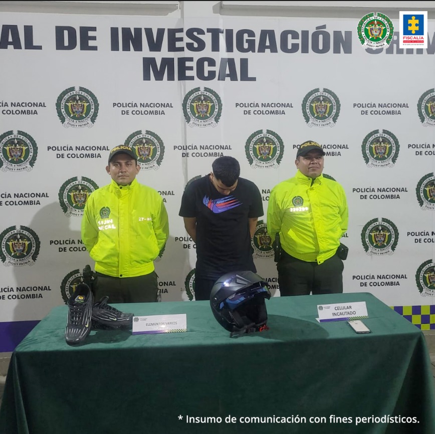 En la foto se aprecia de pie, con la cabeza agachada y los brazos atrás a Luis Eduardo Ramírez Hoyos, alias Nepe. Viste camiseta de manga corta color negra con estampado en la parte frontal; así como pantalón negro. A lado y lado de él hay uniformados de la Policía Nacional. Delante de ellos hay una mesa con mantel verde y sobre ella un casco, unas zapatillas negras y un teléfono celular. Detrás de ellos hay un pendón institucional.