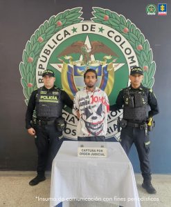 En la fotografía aparece de pie y con los brazos atrás Luis Ernesto Rodríguez González. Usa bigote legeramente poblado y ‘chivera’. Viste con buso de color blanco y estampados rojos y negros. También usa camándula en el cuello de color negro; también pantalón de color gris oscuro. En sus extremos hay uniformados de la Policía. Delante de ellos hay una superficie y sobre ella hay un letrero que dice: ‘Captura por orden judicial’. Detrás de ellos está el escudo de la Policía.