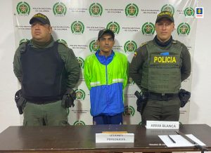 En la foto se aprecia de pie, con los brazos atrás, Luis Francisco Moreno Rengifo. Viste con gorra oscura, chaqueta de sudadera verde fluorescente y azul; pantalón oscuro. A lado y lado de él hay uniformados de la Policía Nacional. Delante de ellos hay una superficie marrón y sobre ella se aprecian un cuchillo y un machete. Asimismo, un letrero que dice: ‘Arma blanca’. Detrás de ellos hay un pendón institucional de la Policía