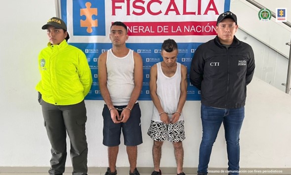 En la fotografía aparece los dos capturados junto a un uniformado de la Policía Nacional y a un investigador de CTI. En la parte posterior se aprecia el banner que identifica la Fiscalía General de la Nación.