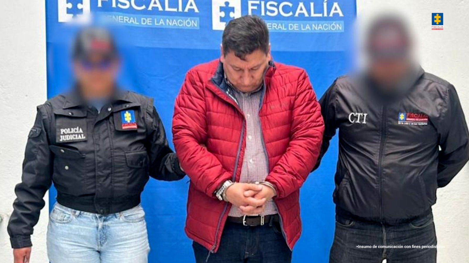 El capturado aparece de pie, con las manos esposadas al frente. Está con la cabeza agachada. Lo rodean dos miembros del CTI de la Fiscalía y hay un banner de la institución al fondo. 