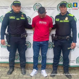 En la imagen aparece una persona de camiseta roja entre dos uniformados de la Policía Nacional. 