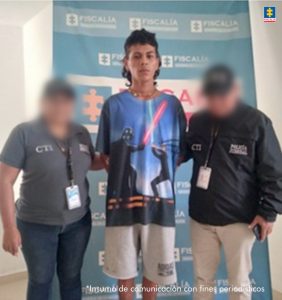 En la imagen aparece un joven con bermuda blanca y camiseta de figuras, en medio de dos uniformados del CTI, de la Fiscalía.